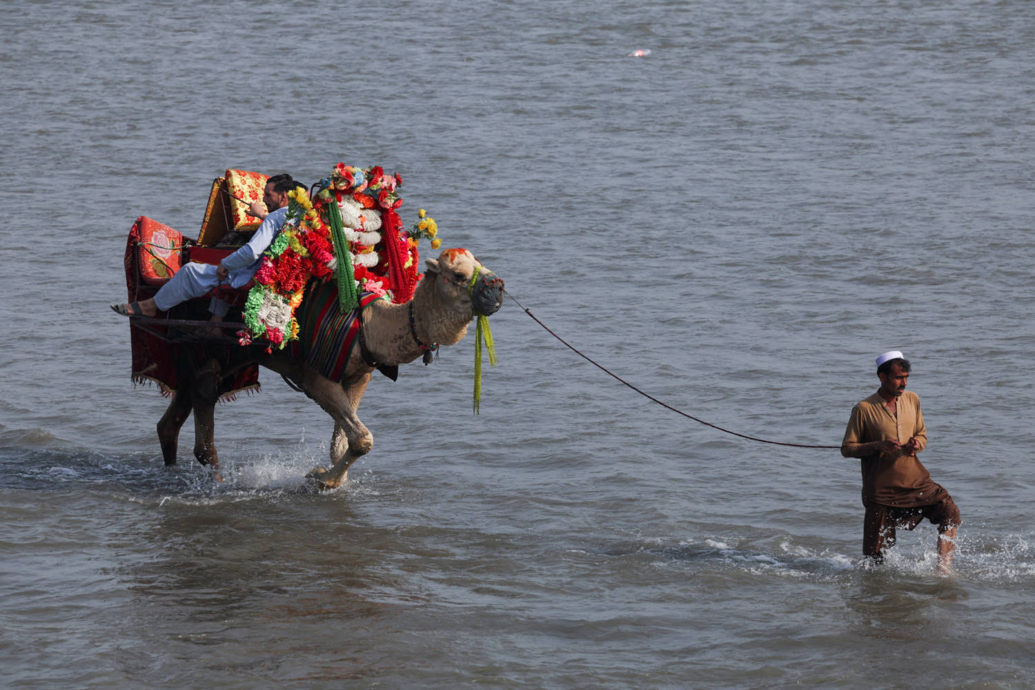 A man leads a camel with men taking a ride on it during the second day of Eid al-Fitr celebrations